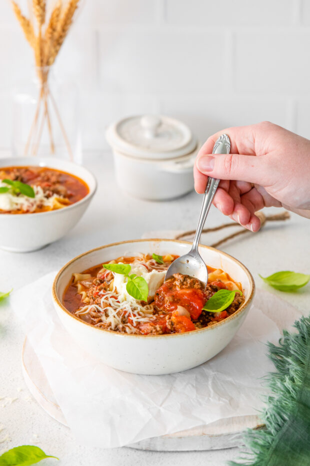 A spoon going into a bowl of lasagna soup.