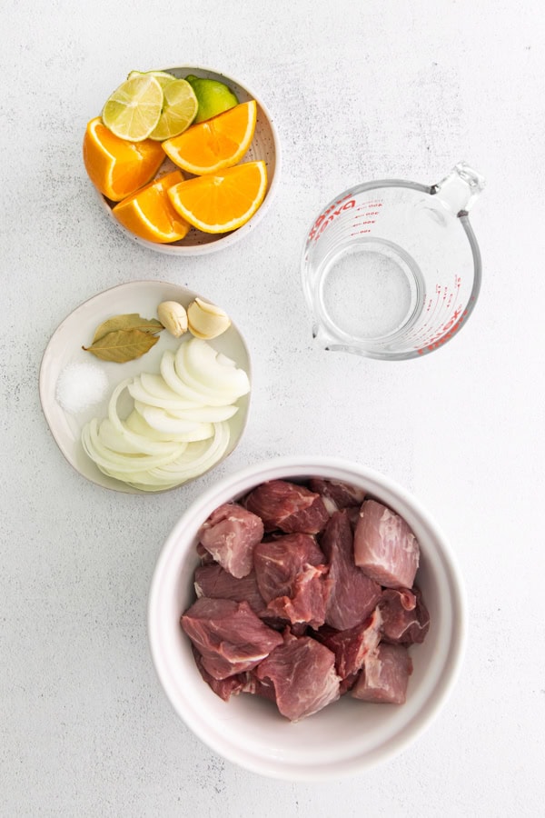 Cubed pork, onions, spices, water, and citrus fruit on a table.