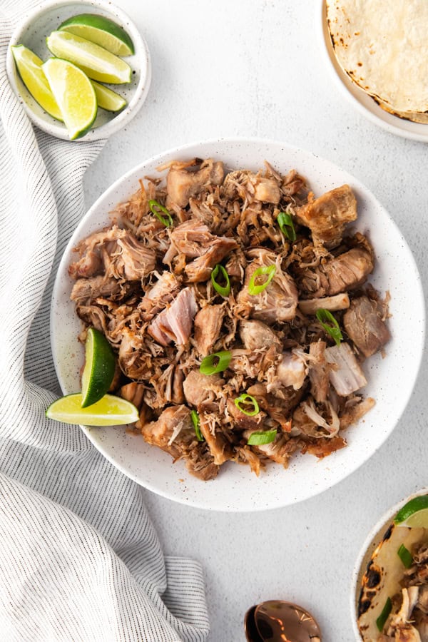 Slow Cooker Pork Carnitas served with lime and green onions.