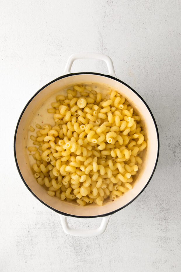 White Cheddar Mac and Cheese in a dutch oven getting stirred. 