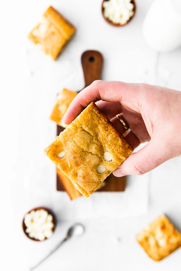 A hand holding a White Chocolate Chip Blondie. 