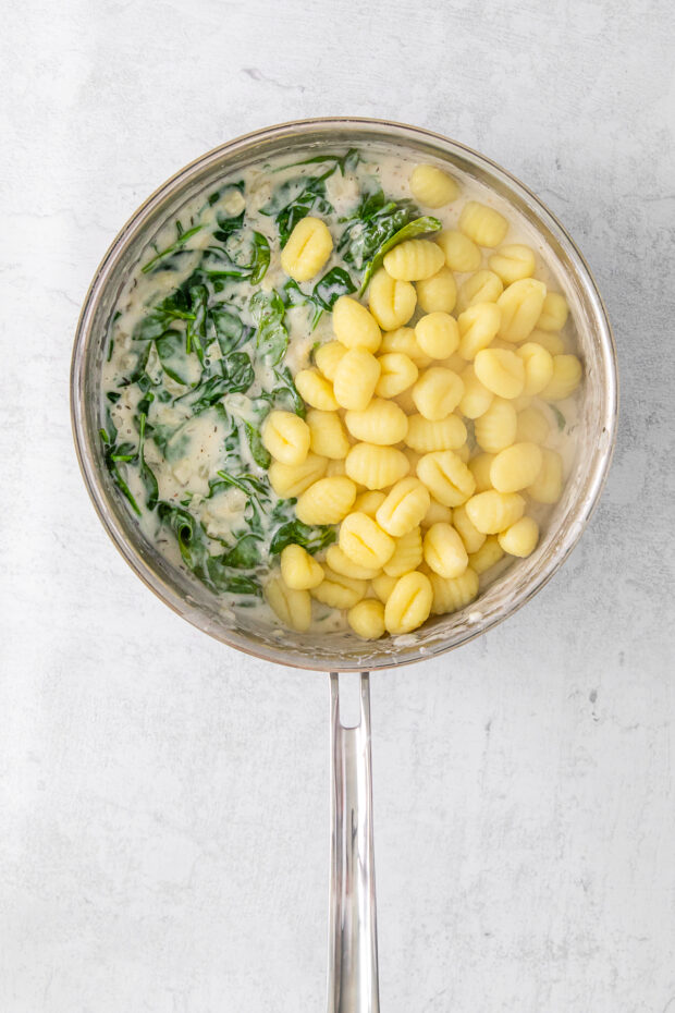 Creamy spinach sauce with gnocchi in a skillet.