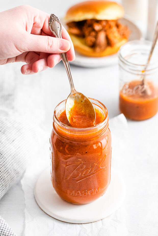 A spoon taking some bbq sauce out of jar.