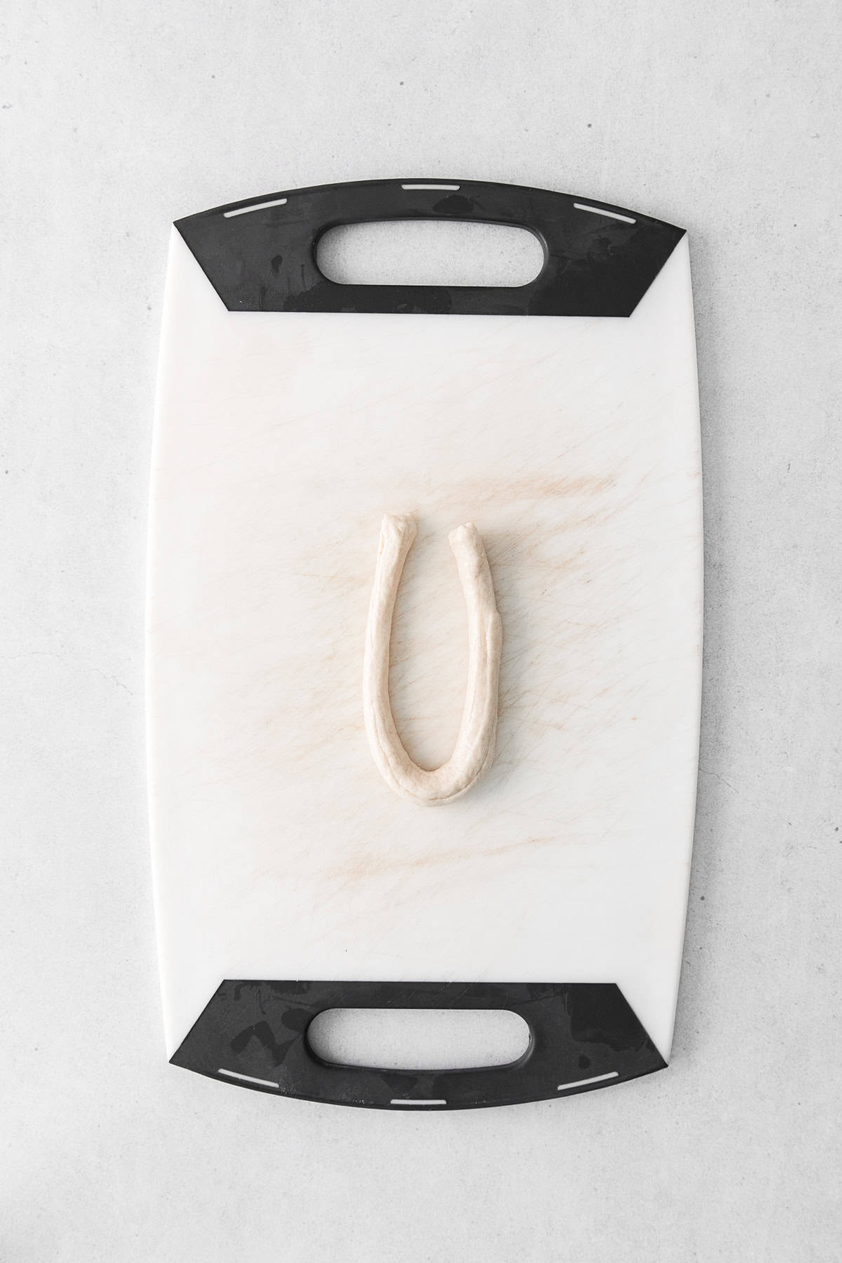 A piece of soft pretzel dough in a U shape on a cutting board.