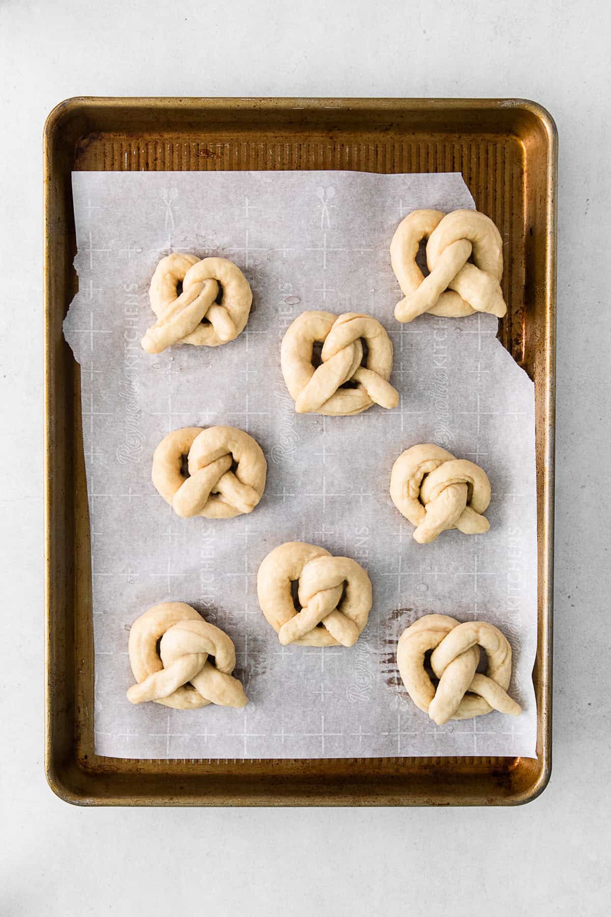 Folded soft pretzels uncooked on a baking tray.