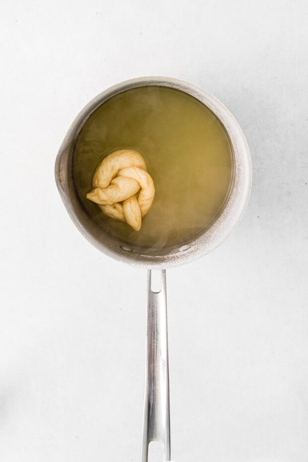 A pretzel being boiled in baking soda water.