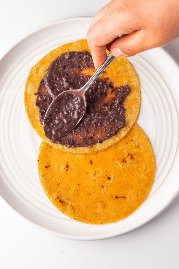 Spreading refried black beans on a tortilla. 