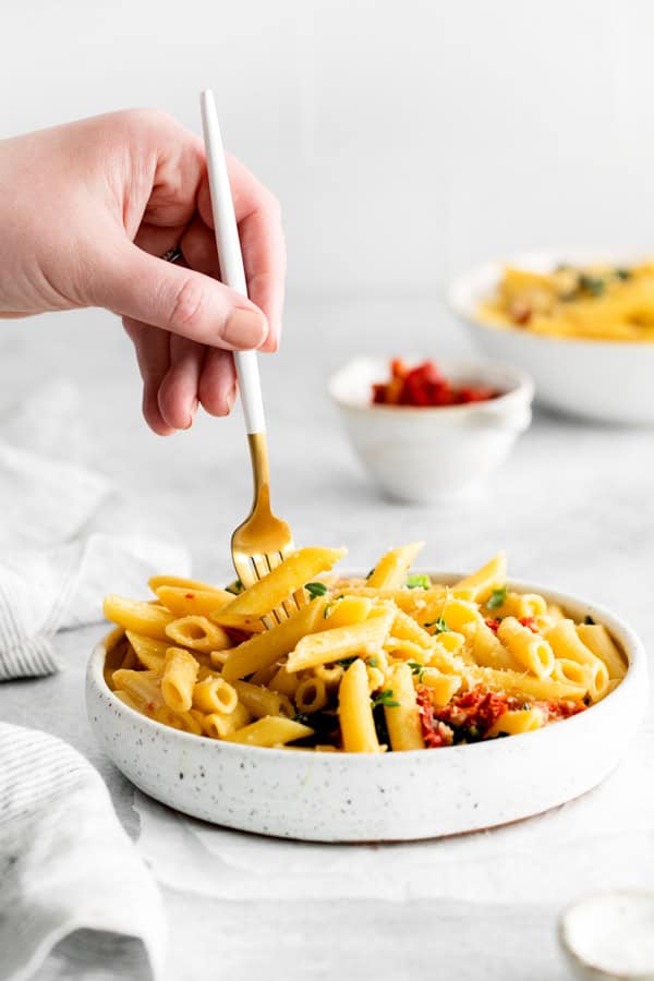 A hand holding a fork picking up a bite of Sun dried Tomato and Kale Pasta.