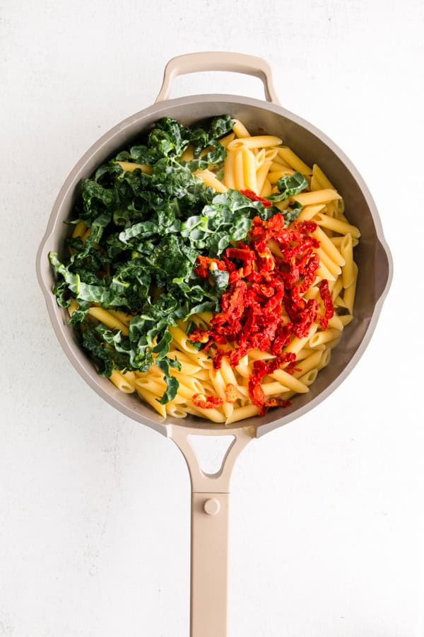 Pasta with sun dried tomatoes and kale in a skillet.