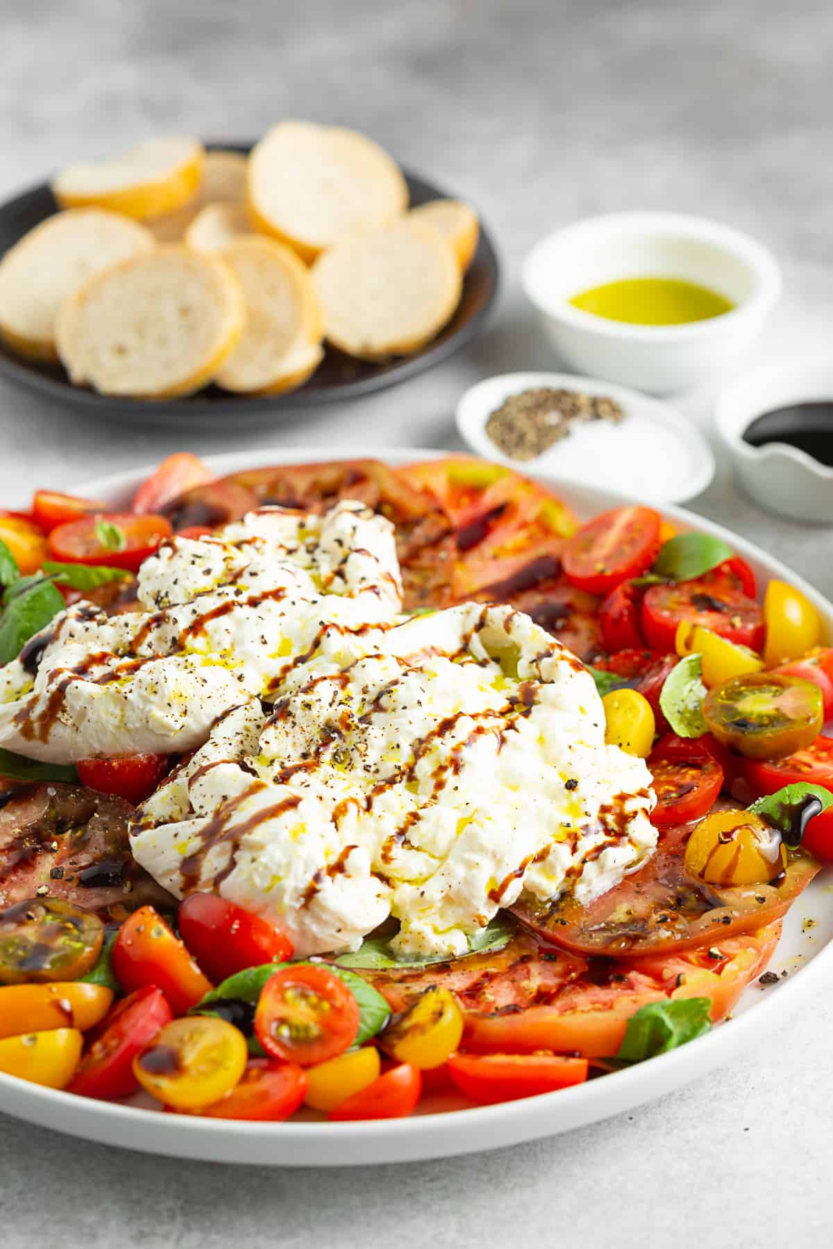 Burrata Caprese Salad on a table with bread and olive oil. 