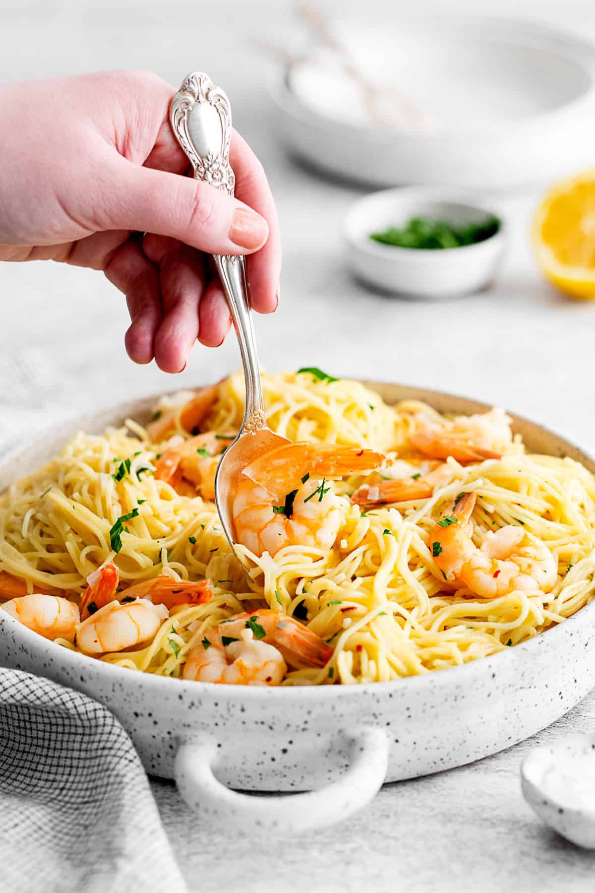 A spoon picking up a shrimp out of shrimp scampi. 