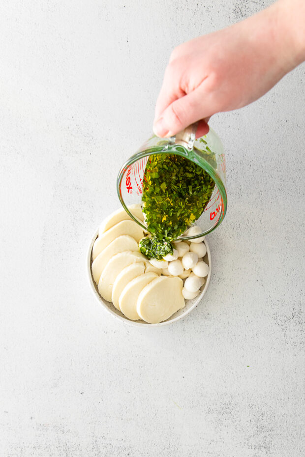 Pouring olive oil and herbs over mozzarella cheese. 