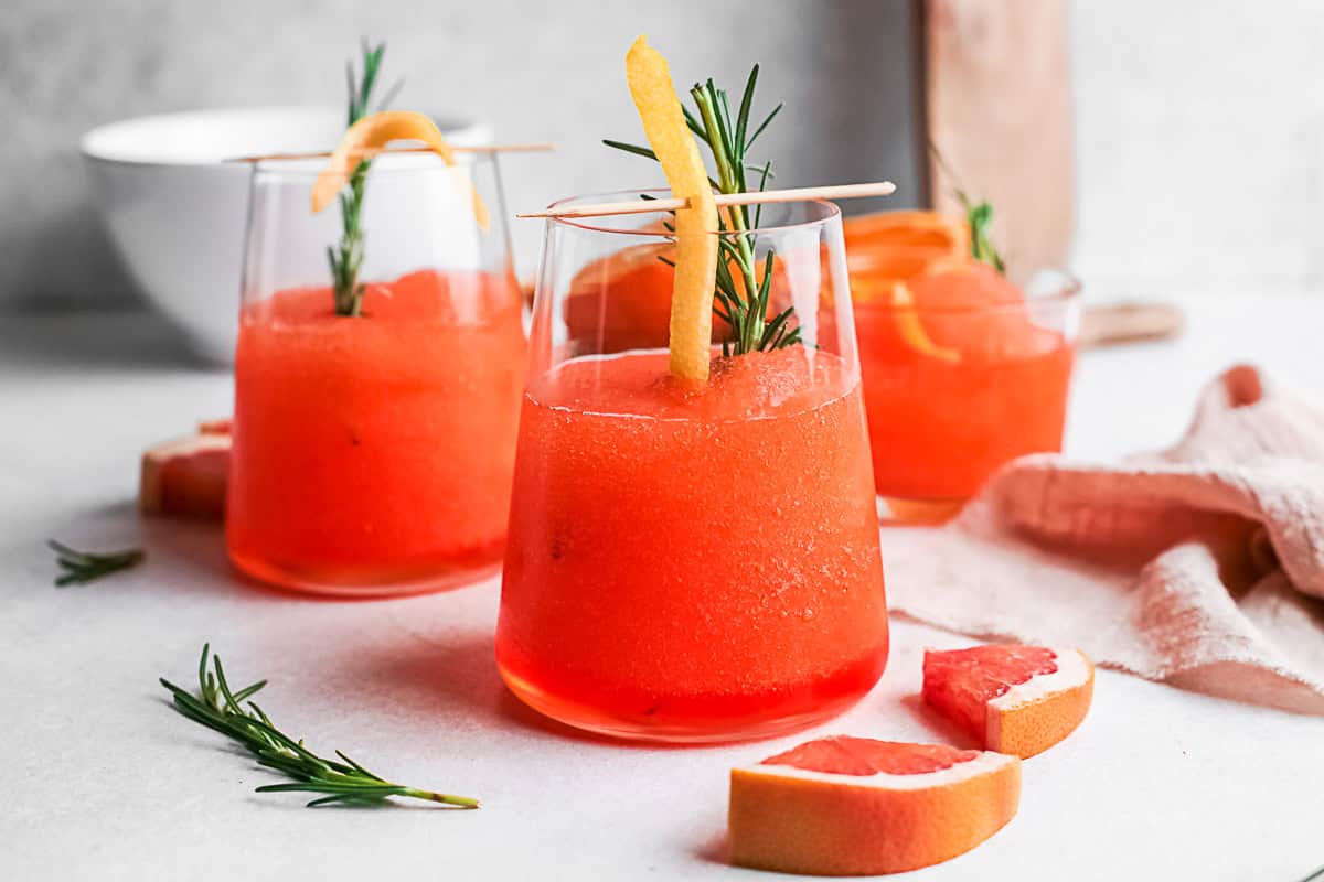 Frozen Aperol Spritz sitting on a table with sliced fresh citrus. 