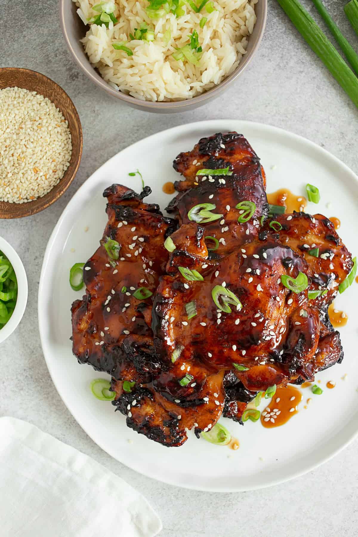 Grilled Teriyaki Chicken on a white plate topped with sesame seeds and green onions.