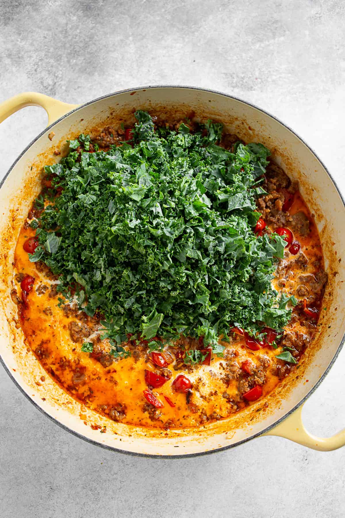 Adding kale to a skillet of creamy tomato sauce. 