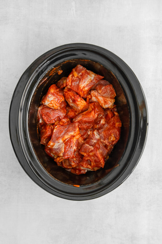 Chunked pork shoulder with seasoning in a slow cooker. 
