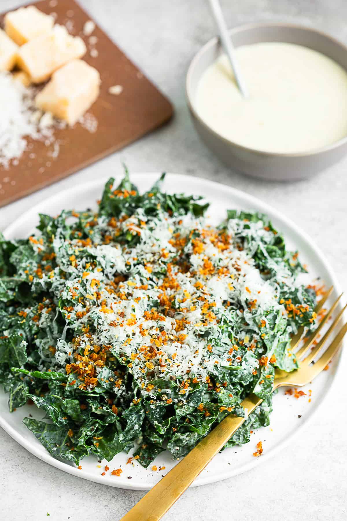 Chopped Kale Caesar Salad on a plate with extra dressing and cheese. 