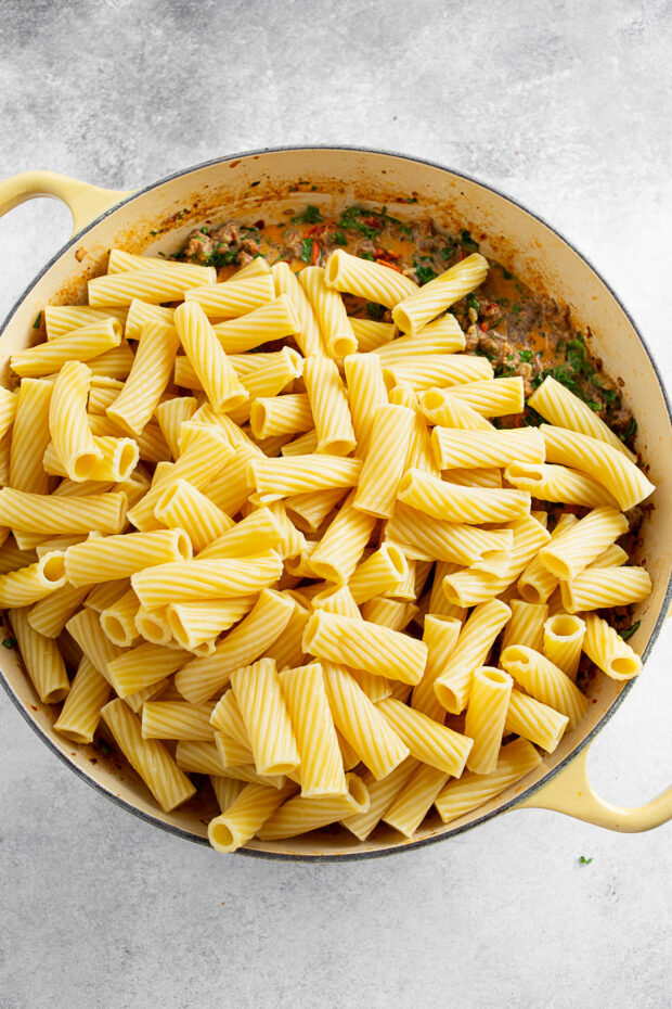 Adding pasta to a dish of creamy tomato sauce. 