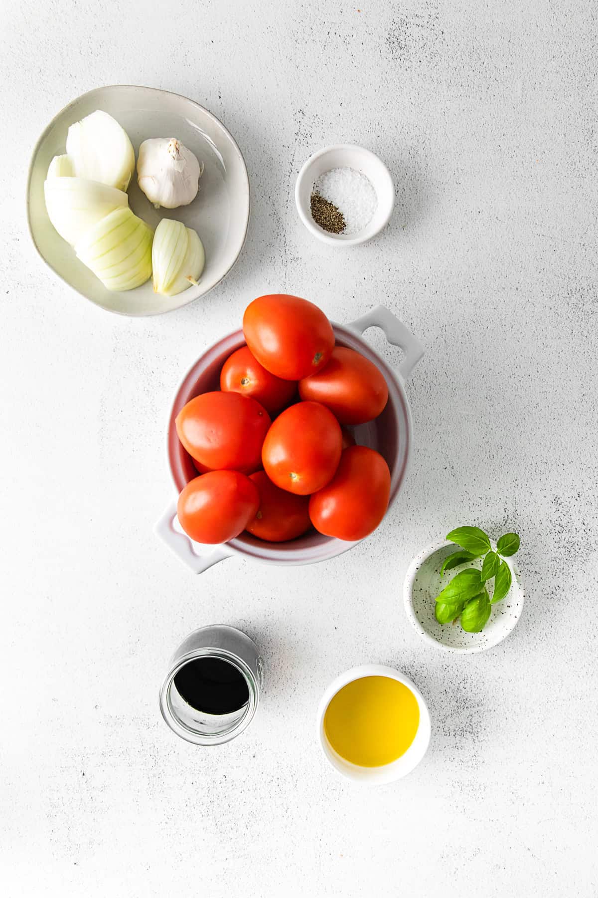 Onion, garlic, tomatoes, olive oil, basil balsamic vinegar and kosher salt on a table. 
