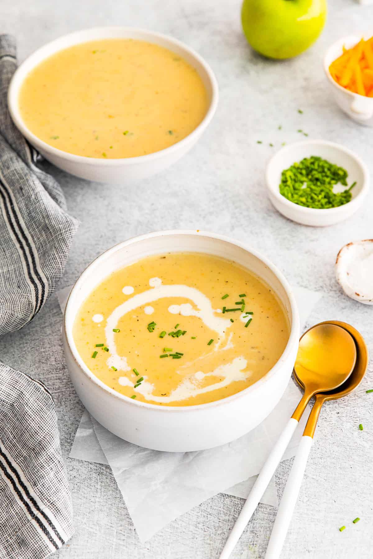 Apple Cheddar Soup sitting on a table with another bowl of soup in the background. 