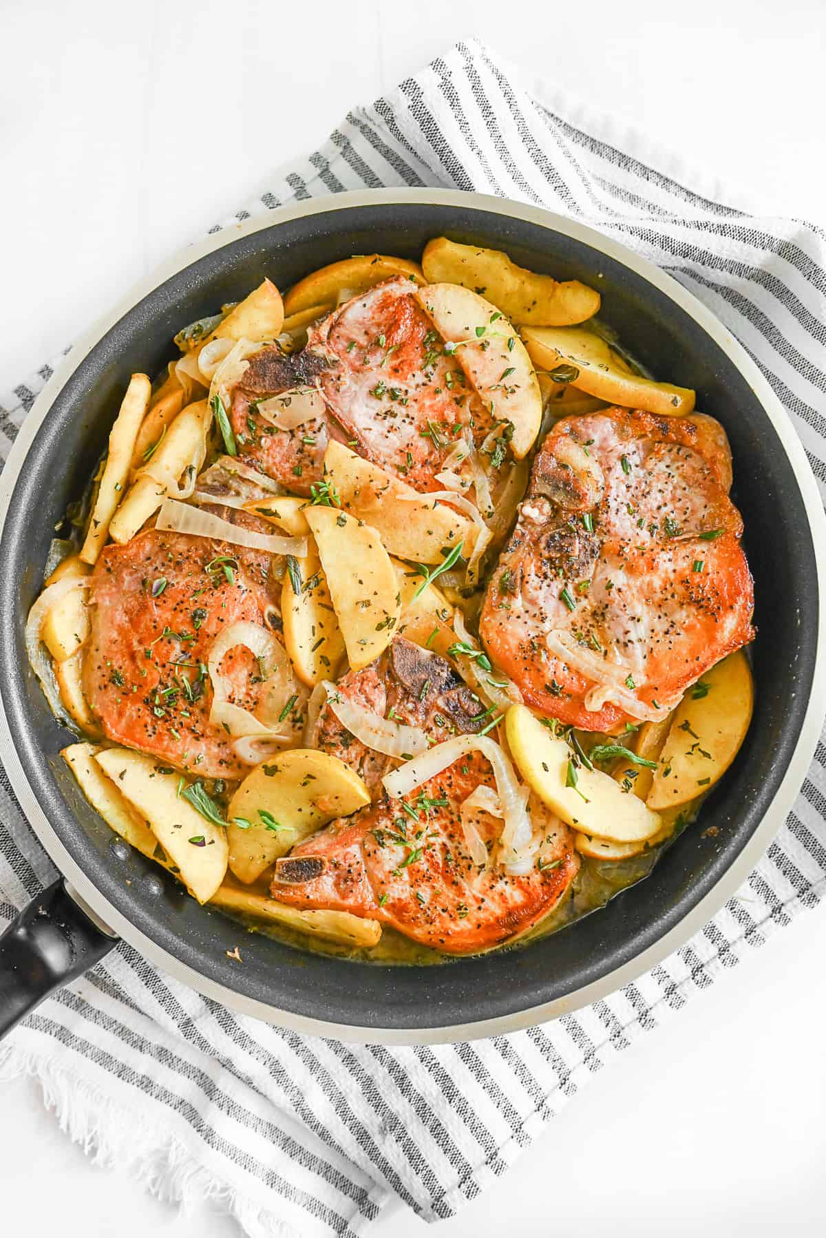Pork Chops with Apples in a skillet with extra apples on top. 