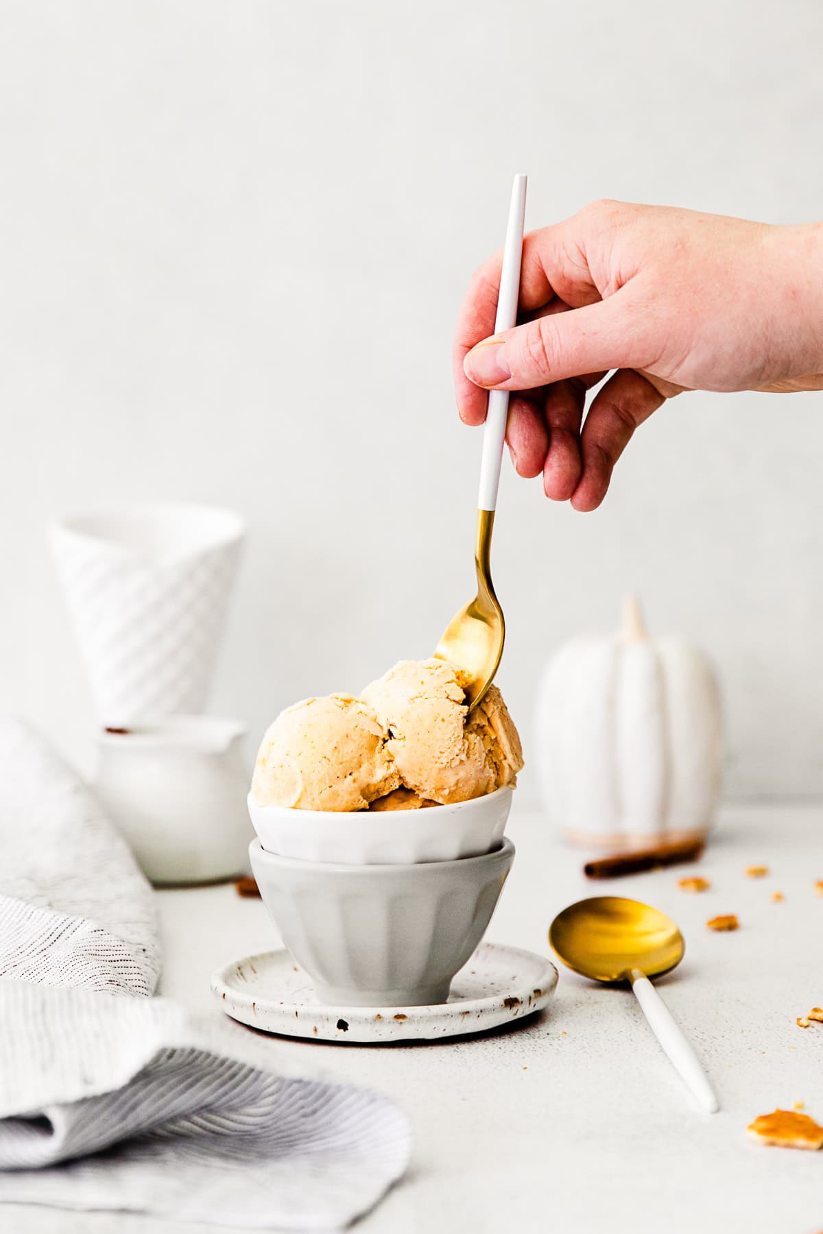 A hand holding a spoon digging into a bowl of No-Churn Pumpkin Pie Ice Cream.
