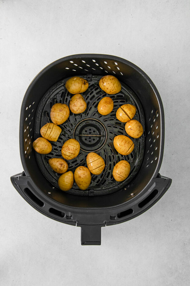 Uncooked potatoes in an air fryer basket.
