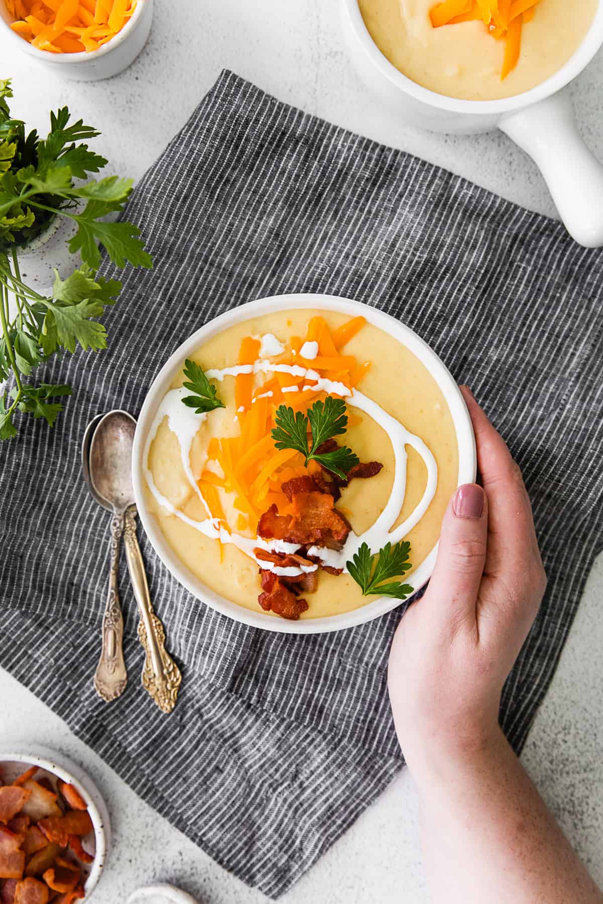 A hand holding a bowl of Instant Pot Loaded Potato Soup. 