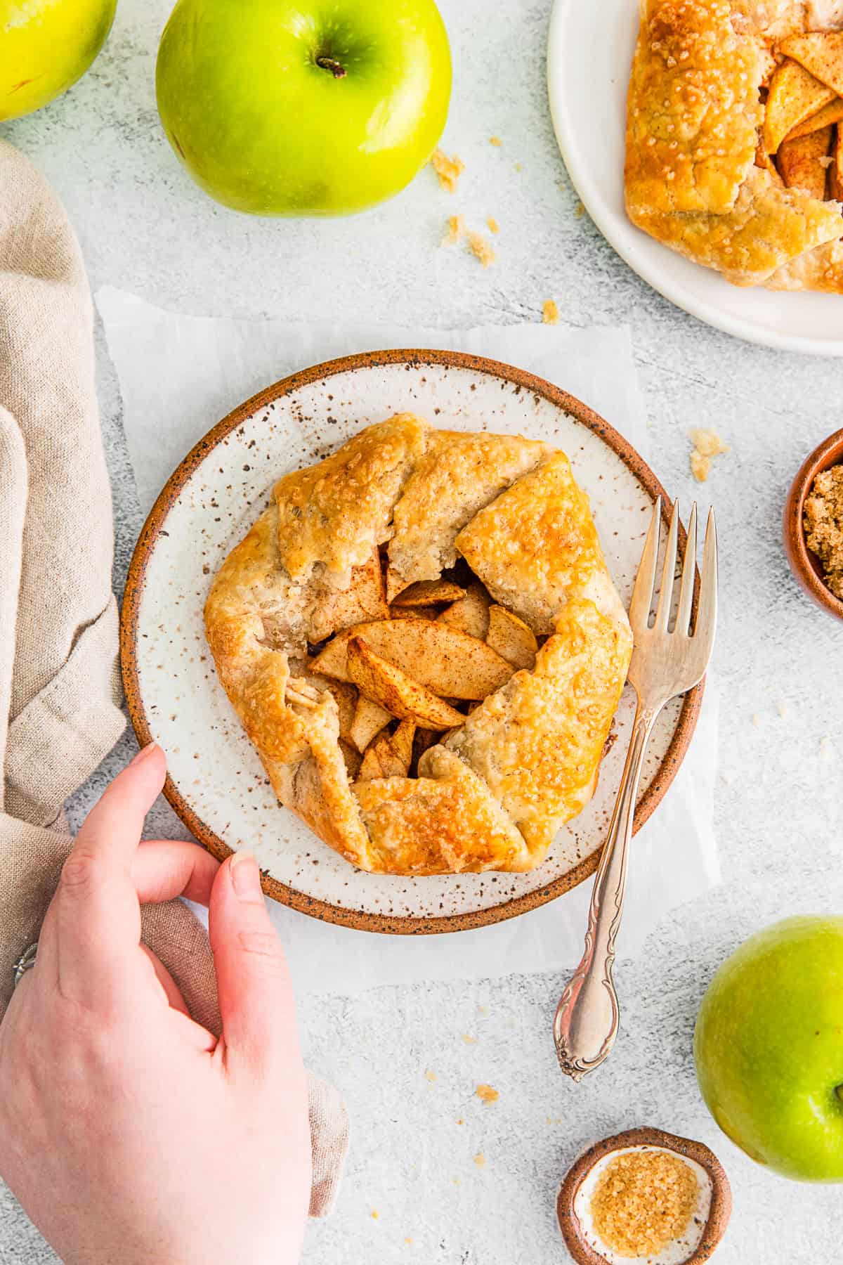 A hand holding a plate with a mini apple galette on it. 