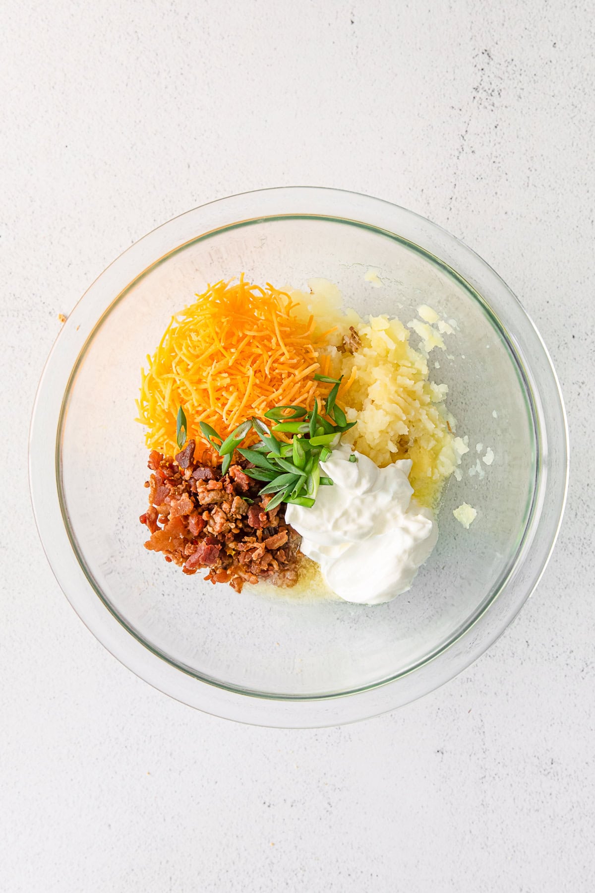 Potatoes, sour cream, cheese, bacon and chives in a bowl. 