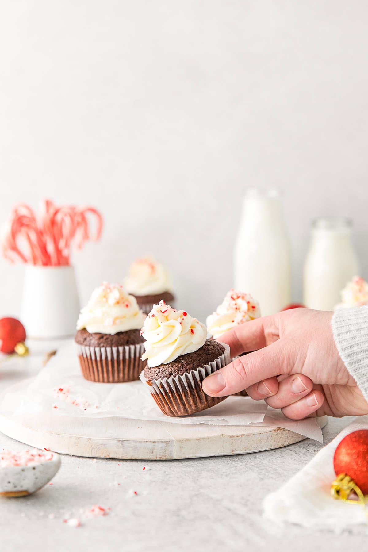 A hand picking up a Peppermint Bark Cupcake. 