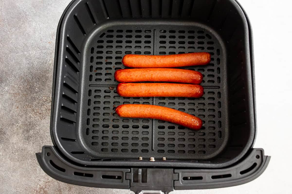 cooked hot dogs in an air fryer basket.