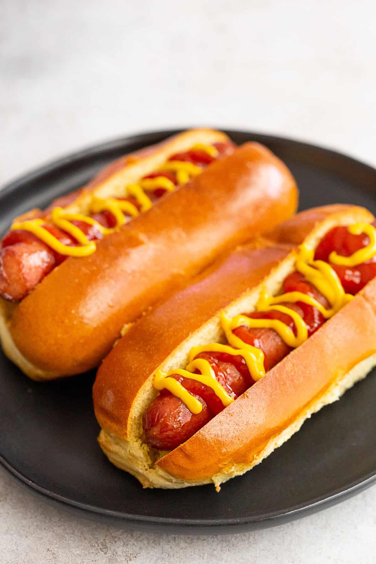 air fryer hot dogs on a plate with yellow mustard and ketchup.
