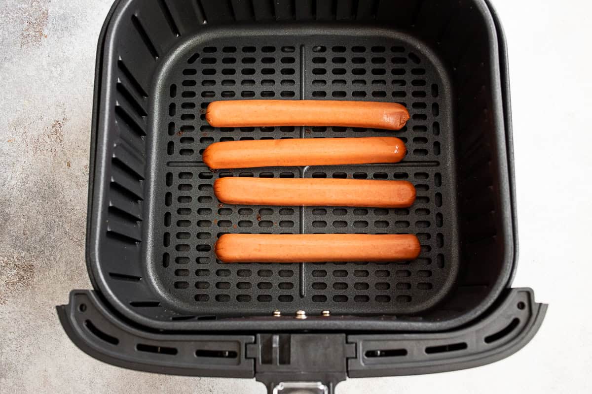 uncooked hot dogs in an air fryer basket.