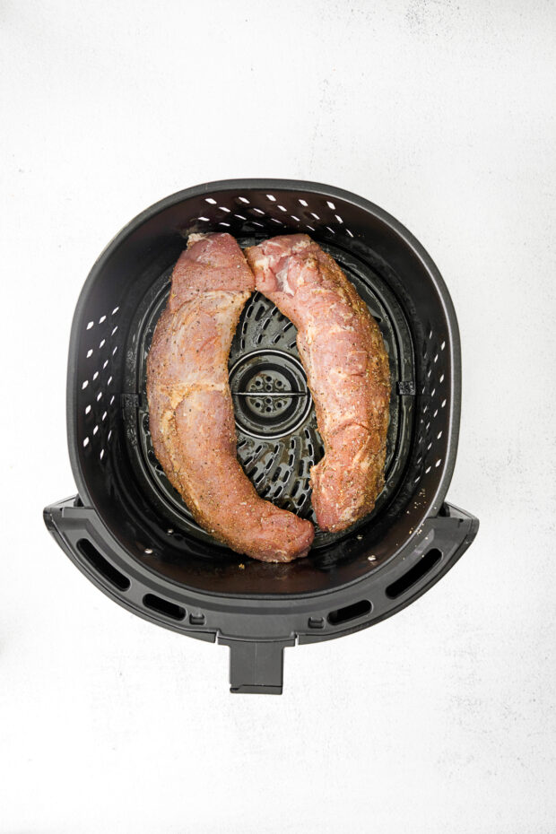 Uncooked pork tenderloin in an air fryer basket. 
