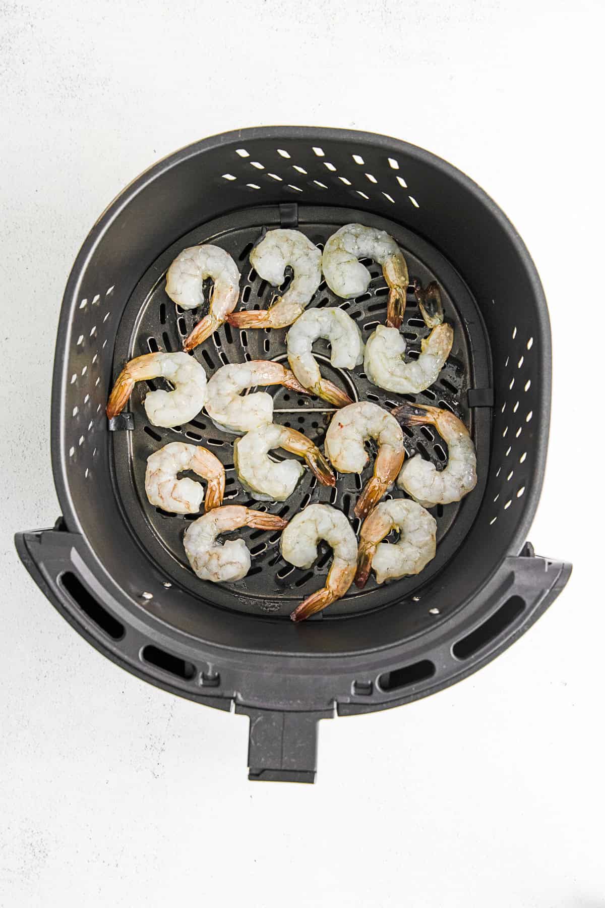 Uncooked shrimp in an air fryer basket.