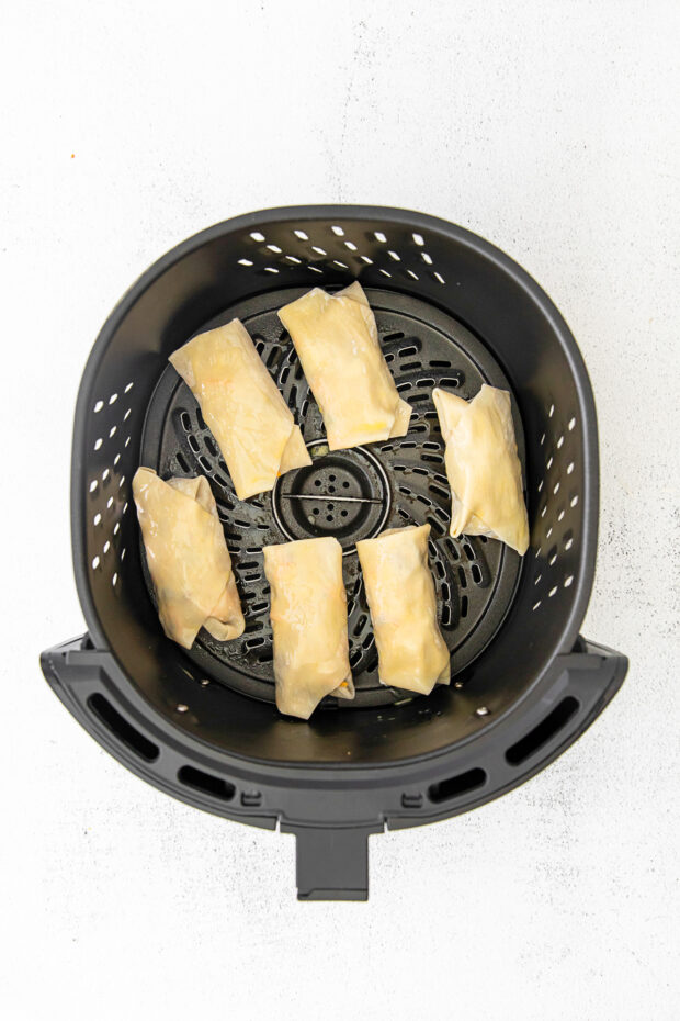 cheeseburger egg rolls in an air fryer basket.