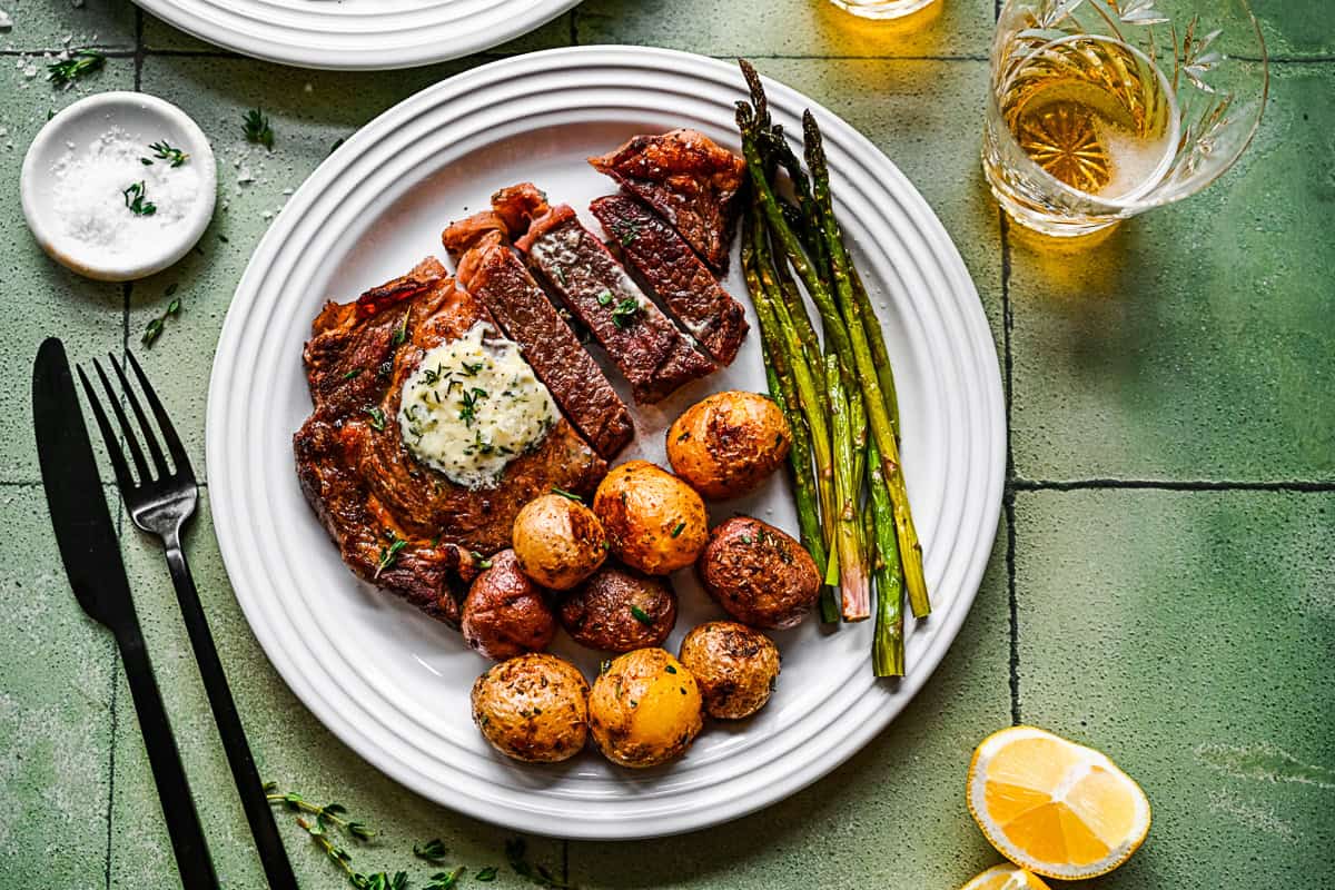 Pan Fried Ribeye on a white plate with potatoes and vegetables. 