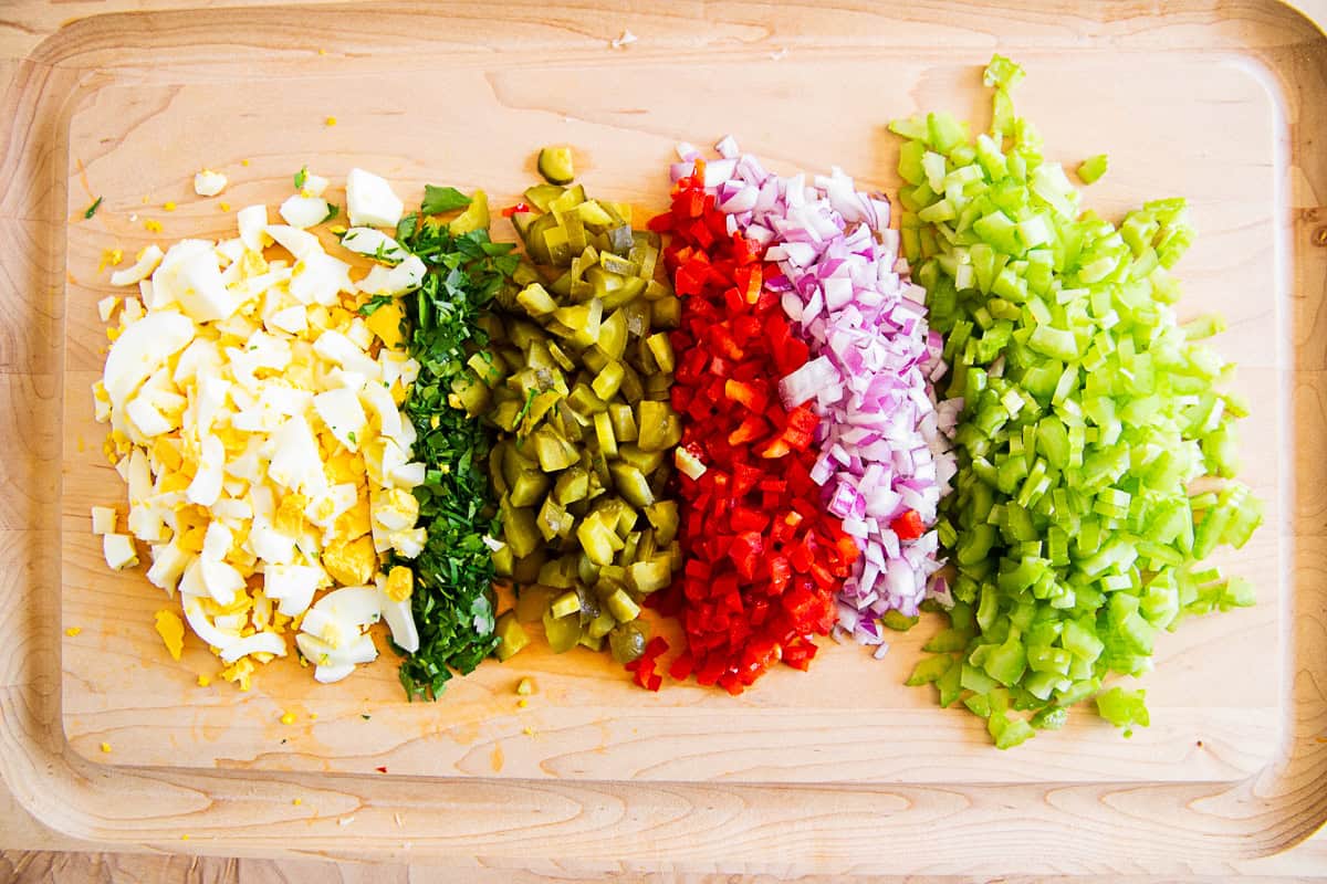 Chopped celery, red onion, red bell pepper, pickles, parsley, and egg on a cutting board. 