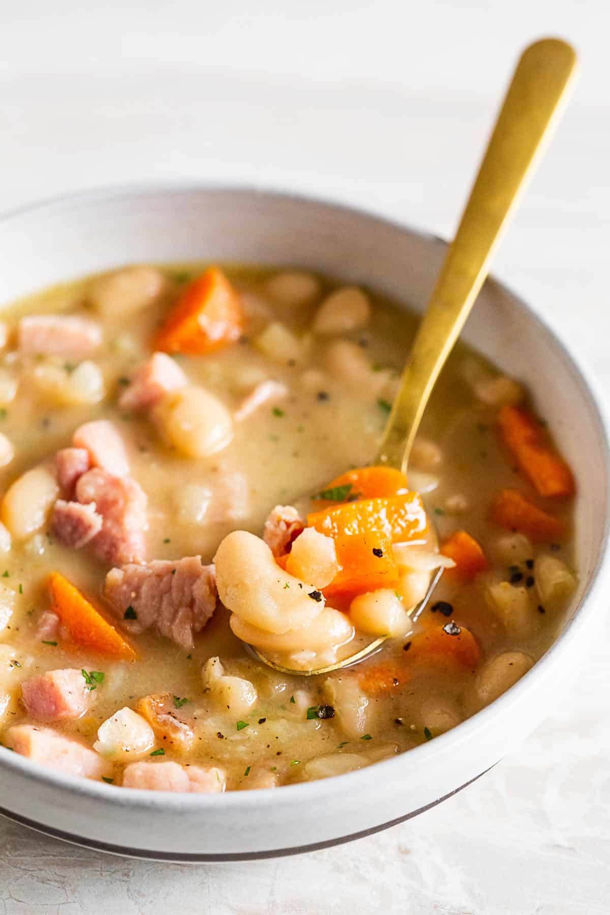 A spoon with a spoonful of ham and bean soup. 