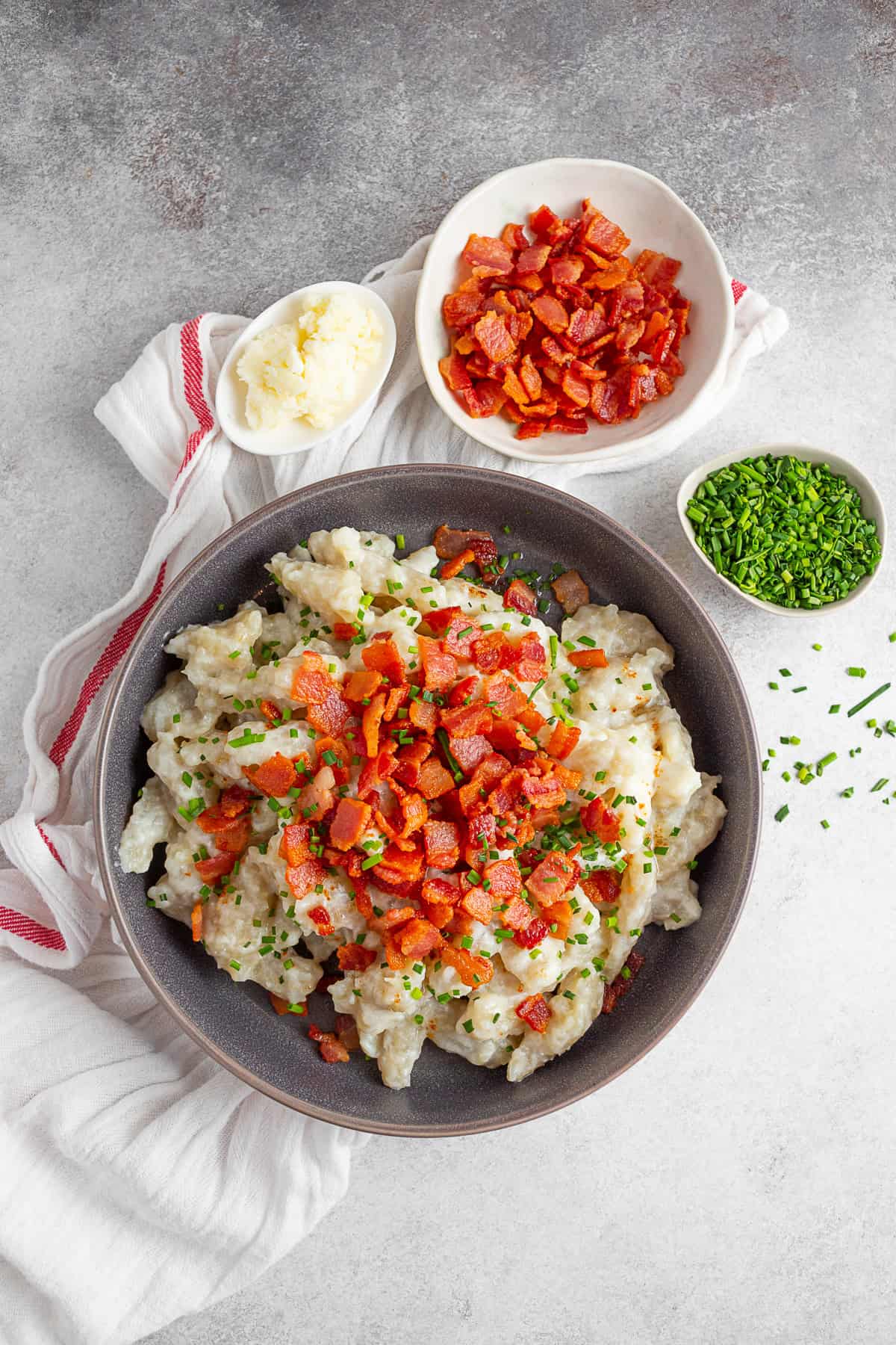 Potato Halusky (Bryndzové halušky) on a table surround by extra bacon. 