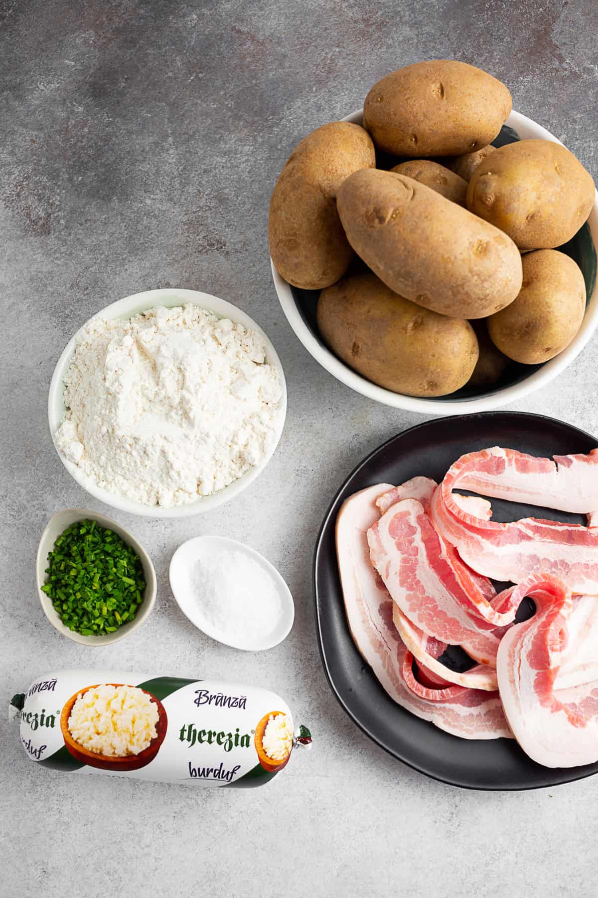 Potatoes, flour, bacon, chives, kosher salt, and cheese on a table. 