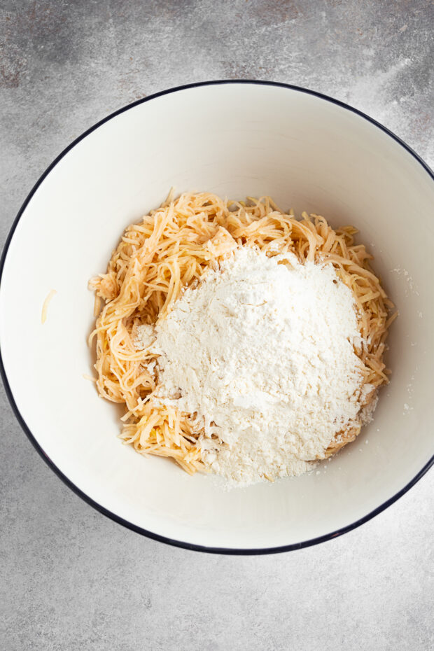 Shredded potatoes and flour in a bowl. 