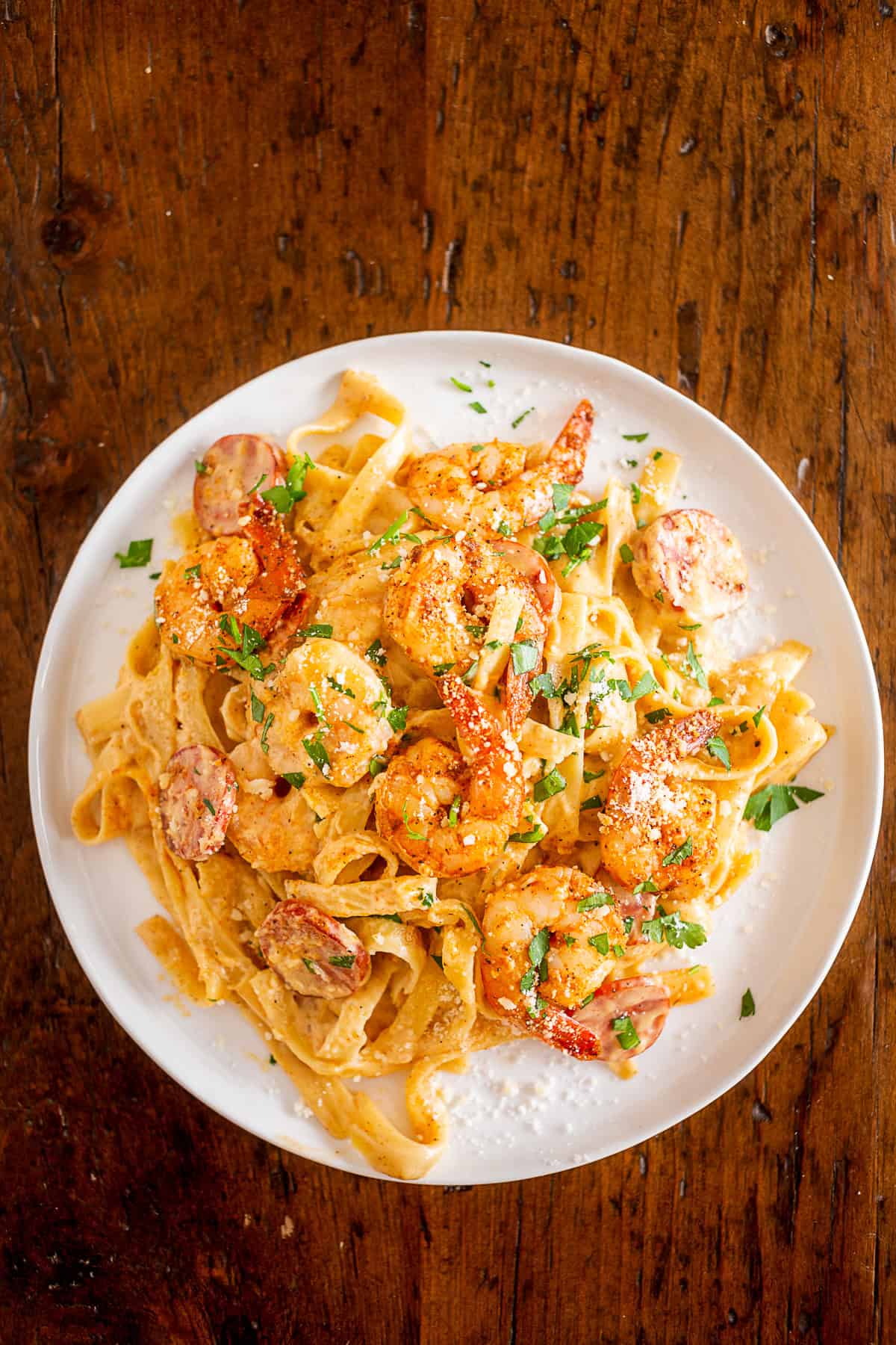 cajun shrimp fettuccine alfredo served on a white plate sitting on a wooden table.