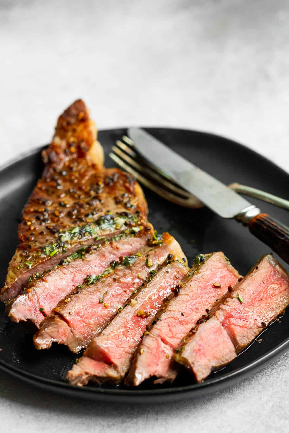 Cast Iron Seared Strip Steak sliced on a plate with a fork and knife. 