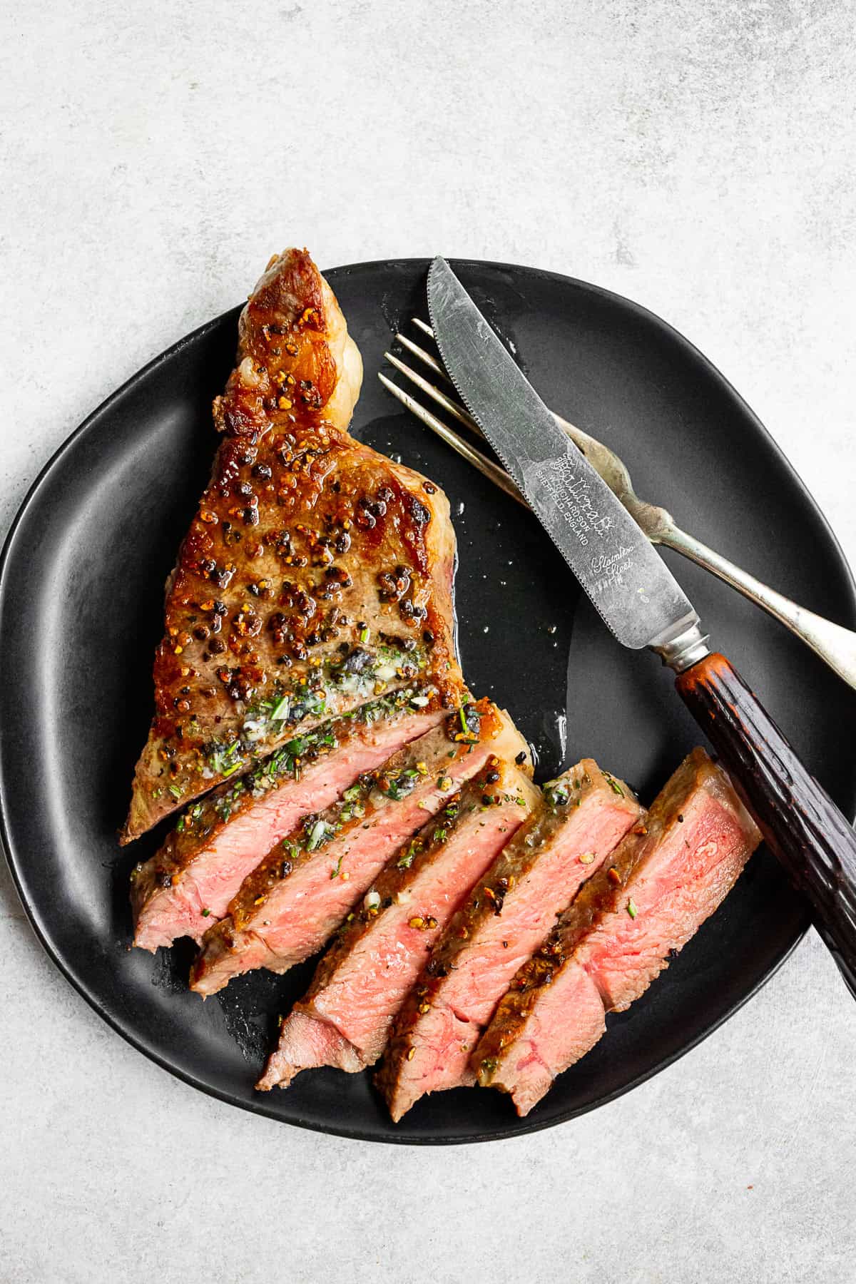 sliced cast iron seared strip steak on a black plate