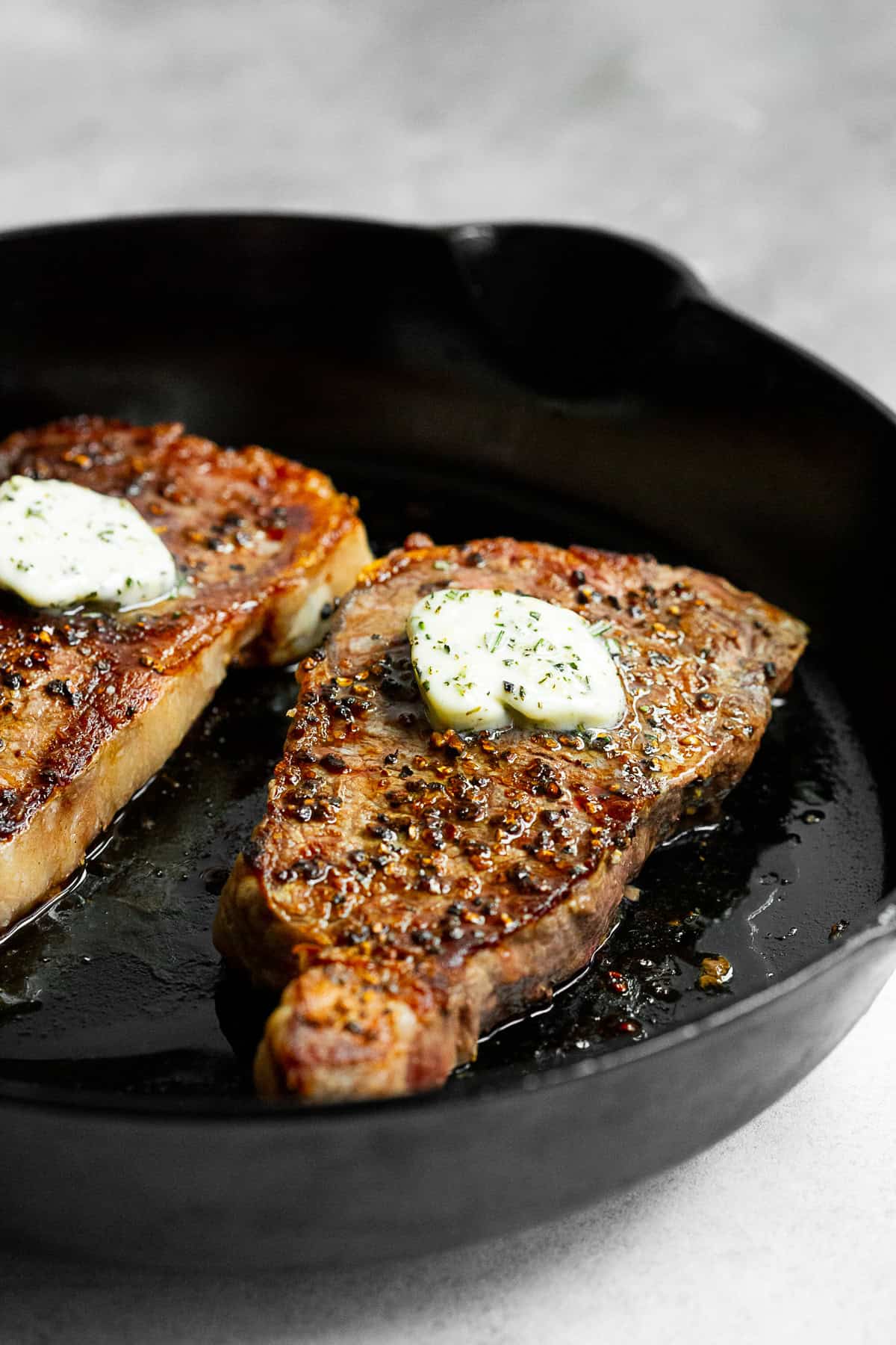 cast iron seared strip steak sitting in the pan with compound butter on top