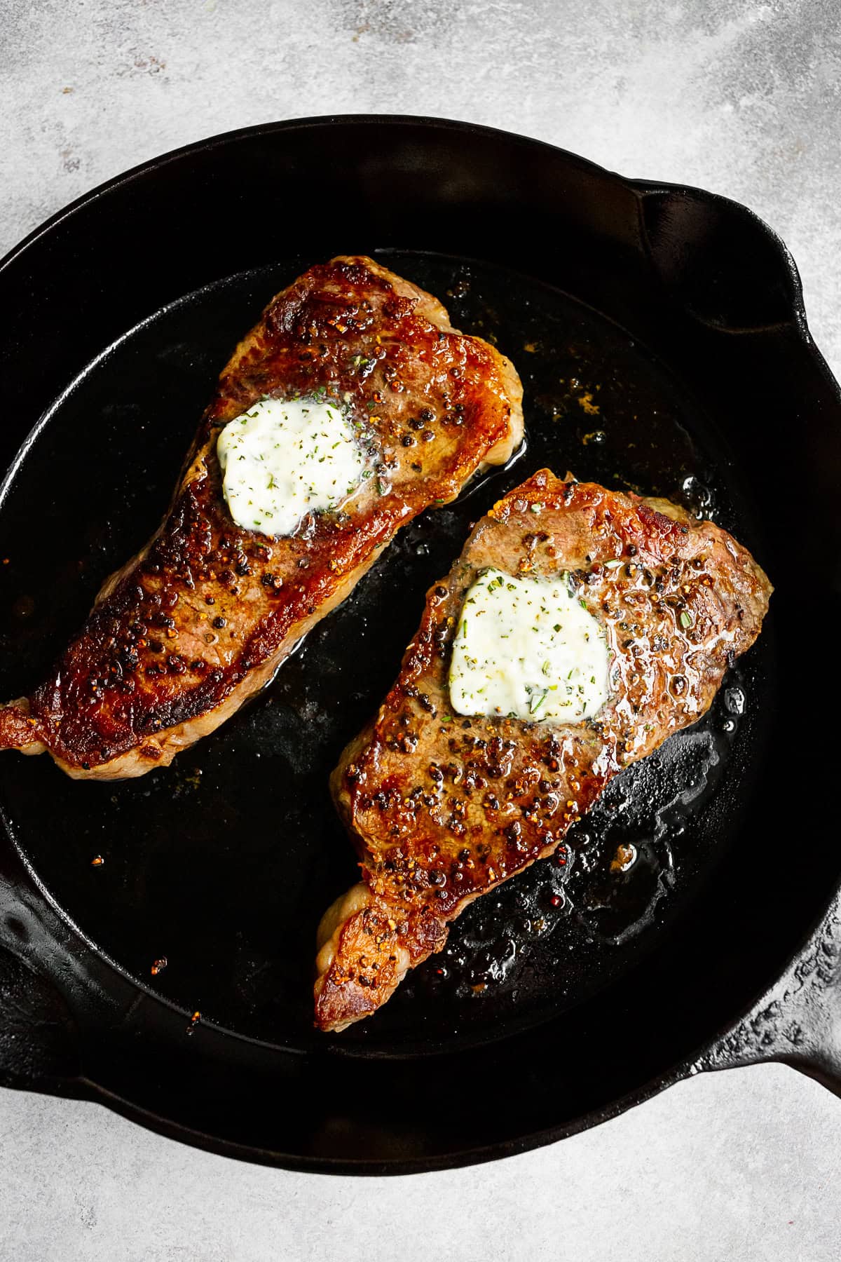 cast iron strip seared strip steak in a pan with butter on top