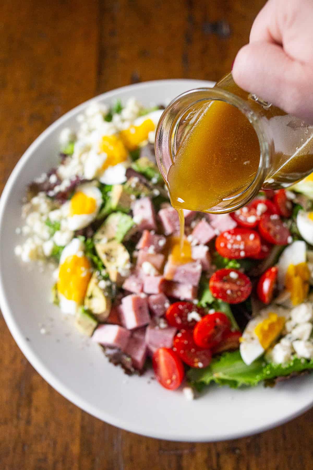 Pouring dressing onto a Ham Cobb Salad.