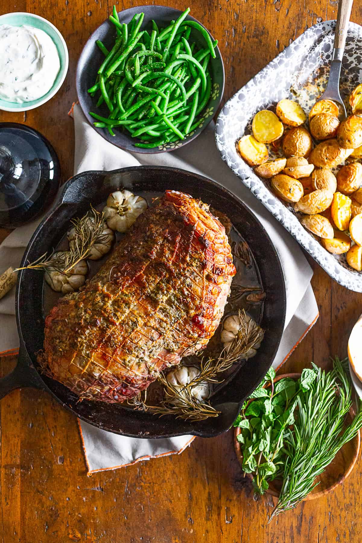 Garlic Rosemary Roast Leg of Lamb on the table surrounded by side dishes. 
